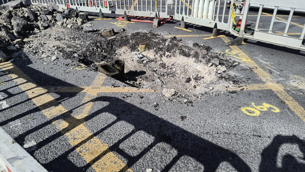 Picture of large hole approx  5 meteres across with two vlack sawn off mains exposed